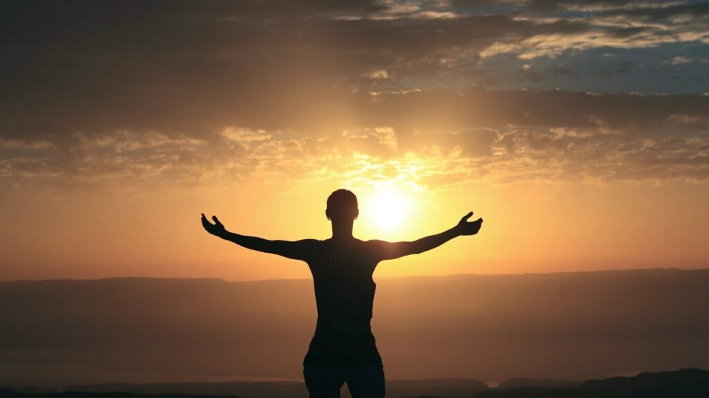 男性が夕日に向かって両手を上げている画像